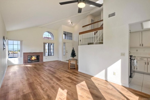 unfurnished living room with visible vents, a brick fireplace, ceiling fan, high vaulted ceiling, and light wood-type flooring