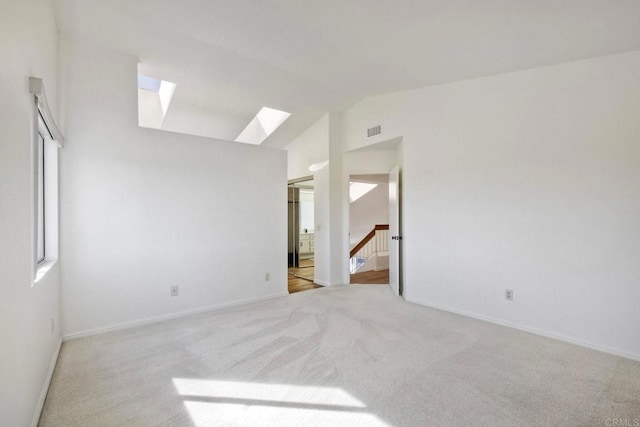 empty room featuring light carpet, lofted ceiling with skylight, visible vents, and baseboards