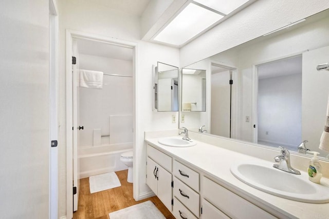 bathroom featuring wood finished floors, a sink, toilet, and double vanity