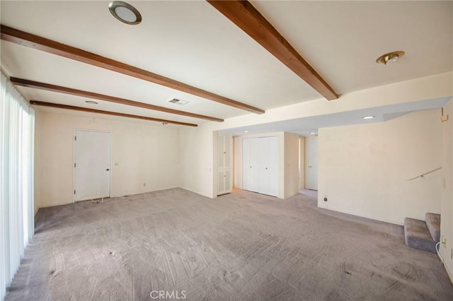 spare room featuring light colored carpet, beamed ceiling, and visible vents