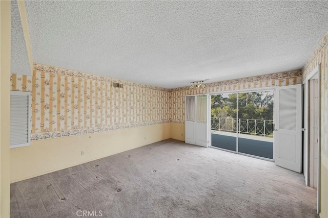 spare room featuring wallpapered walls, a textured ceiling, visible vents, and carpet flooring