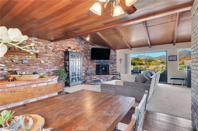 dining area featuring vaulted ceiling with beams, brick wall, wood ceiling, a ceiling fan, and a brick fireplace