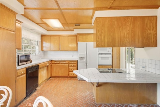 kitchen with black appliances, a peninsula, backsplash, and tile counters