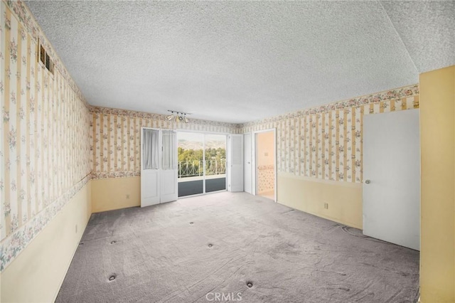 carpeted spare room featuring a textured ceiling and wallpapered walls