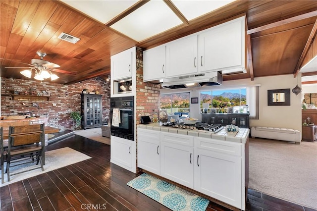 kitchen with tile countertops, visible vents, stainless steel gas stovetop, black oven, and under cabinet range hood