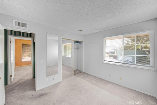 unfurnished bedroom featuring a textured ceiling, a closet, carpet, and visible vents