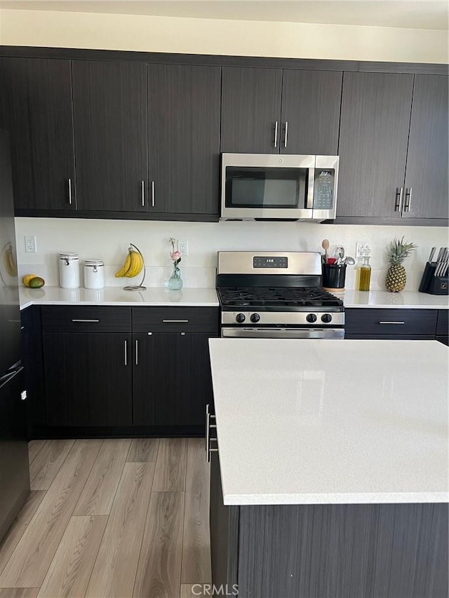 kitchen featuring light wood finished floors, stainless steel appliances, light countertops, modern cabinets, and dark cabinetry