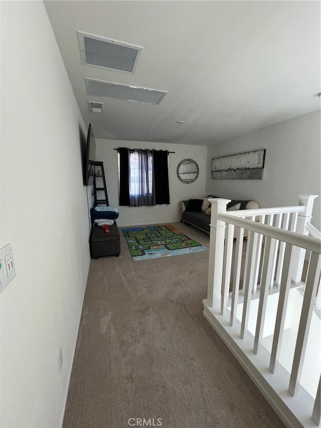 hall featuring carpet floors, visible vents, and an upstairs landing