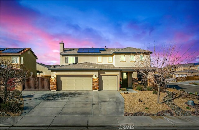 view of front of property with concrete driveway, solar panels, an attached garage, a gate, and stucco siding