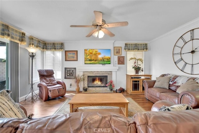 living room featuring light wood finished floors, baseboards, a ceiling fan, a glass covered fireplace, and ornamental molding