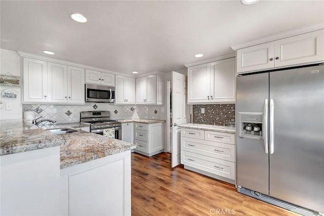 kitchen featuring stainless steel appliances, light wood-type flooring, white cabinetry, and a peninsula