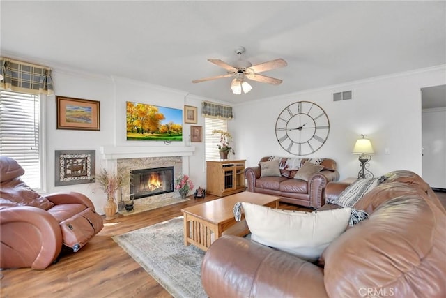 living area with visible vents, a ceiling fan, a premium fireplace, ornamental molding, and wood finished floors