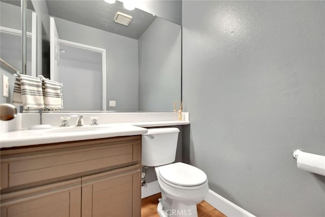 half bath featuring baseboards, vanity, toilet, and wood finished floors