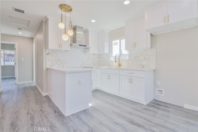 kitchen with decorative light fixtures, light countertops, wall chimney range hood, and white cabinetry