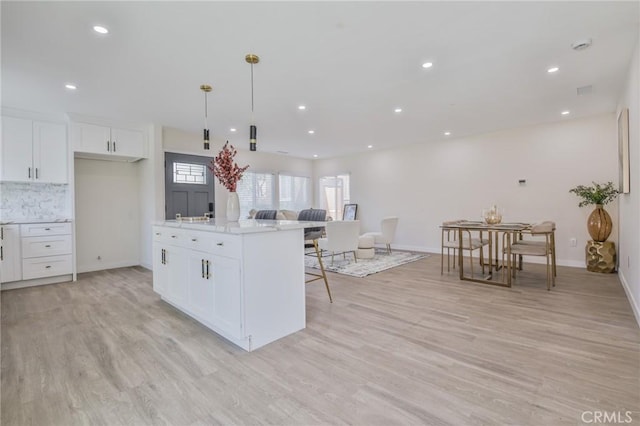 kitchen featuring hanging light fixtures, light wood-style floors, open floor plan, white cabinets, and light stone countertops