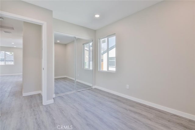 unfurnished bedroom featuring multiple windows, a closet, light wood-style flooring, and baseboards