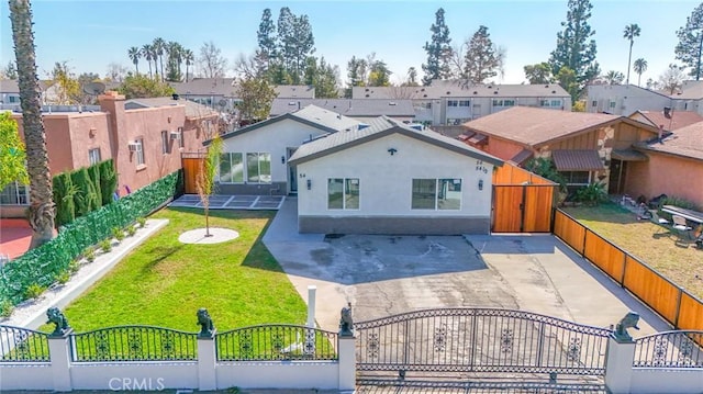 rear view of house with a fenced front yard, a yard, stucco siding, a gate, and a residential view