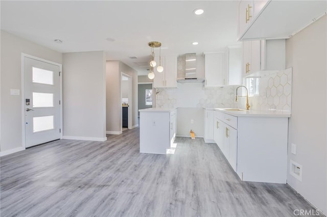 kitchen with wall chimney range hood, white cabinetry, light countertops, and a sink