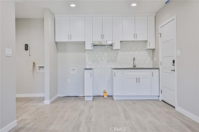 kitchen featuring tasteful backsplash, baseboards, white cabinets, light wood-style flooring, and under cabinet range hood