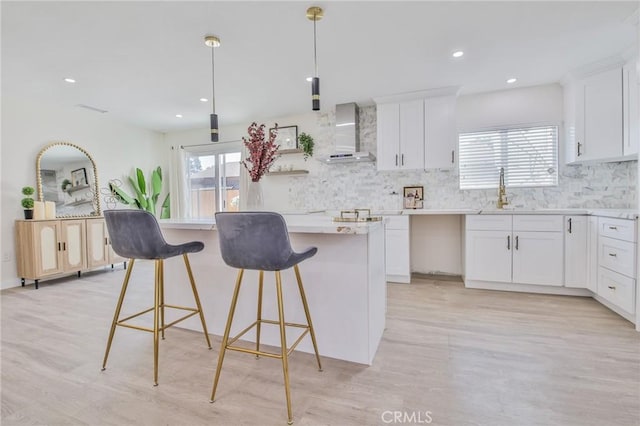 kitchen featuring wall chimney exhaust hood, a center island, white cabinetry, pendant lighting, and backsplash