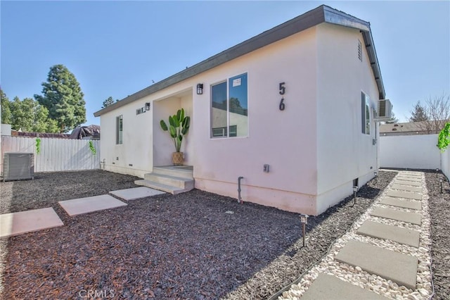 rear view of property with cooling unit, crawl space, fence, and stucco siding