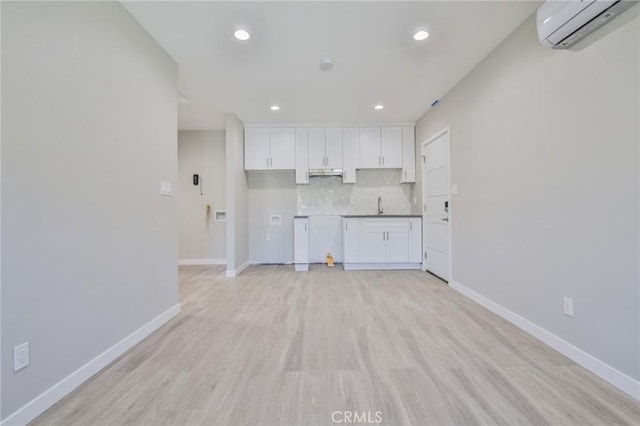 kitchen with baseboards, an AC wall unit, decorative backsplash, and white cabinets