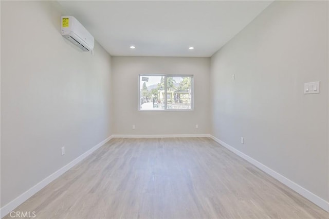 spare room with recessed lighting, a wall mounted AC, light wood-type flooring, and baseboards