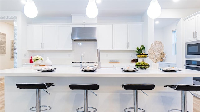 kitchen with under cabinet range hood, an island with sink, light countertops, appliances with stainless steel finishes, and white cabinetry