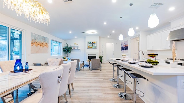 dining room featuring light wood finished floors, visible vents, vaulted ceiling, a fireplace, and recessed lighting