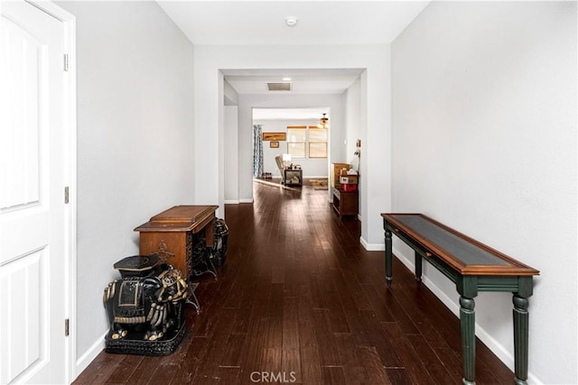 hall featuring dark wood-style flooring, visible vents, and baseboards