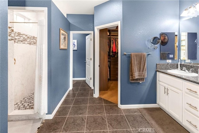 bathroom featuring baseboards, tiled shower, tile patterned floors, a spacious closet, and vanity