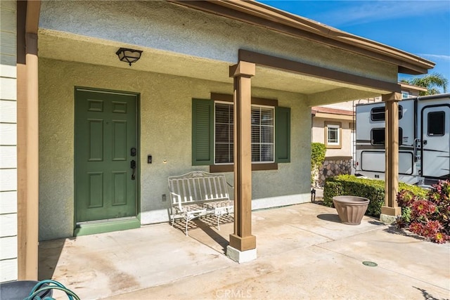 entrance to property featuring covered porch, a patio, and stucco siding