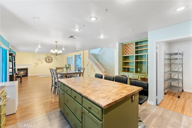 kitchen with decorative light fixtures, a kitchen island, light wood-type flooring, green cabinetry, and a lit fireplace