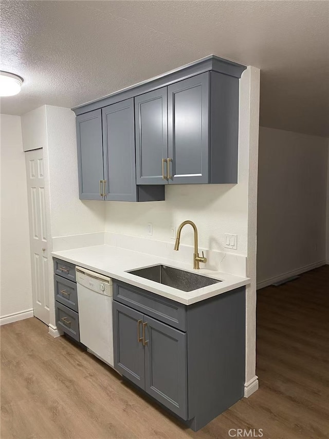 kitchen with white dishwasher, a sink, light wood-style floors, gray cabinets, and light countertops