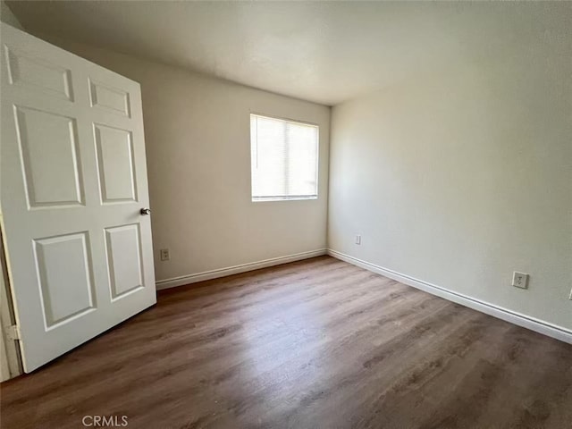 spare room featuring baseboards and dark wood-type flooring