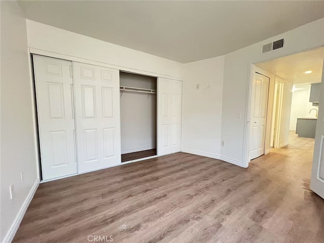 unfurnished bedroom featuring wood finished floors, a closet, baseboards, and visible vents