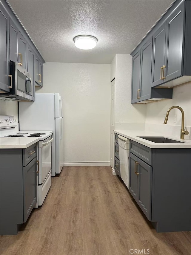 kitchen with light countertops, white appliances, gray cabinets, and a sink