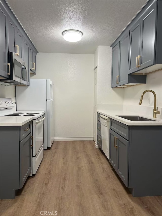 kitchen featuring a sink, a textured ceiling, gray cabinetry, wood finished floors, and white appliances
