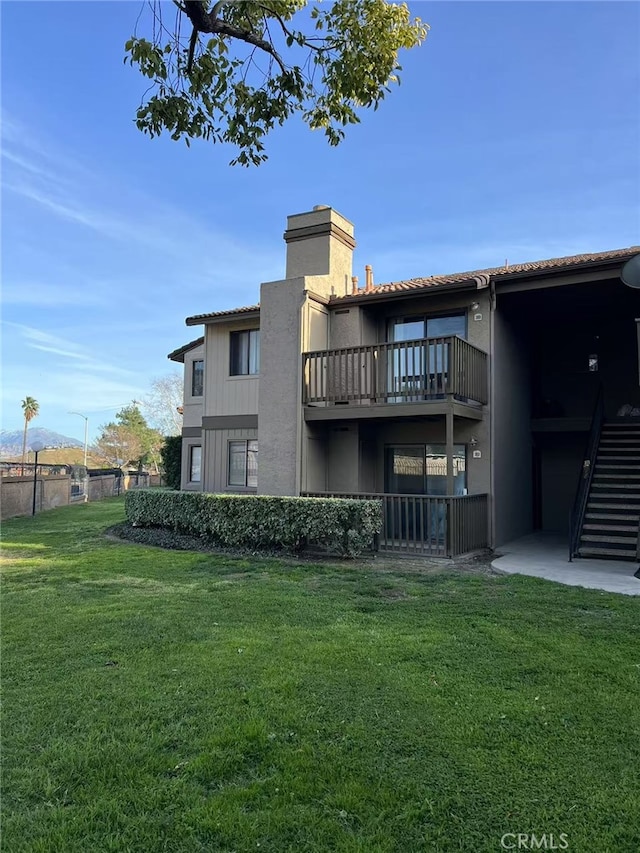 rear view of property featuring fence, a balcony, a yard, and stucco siding