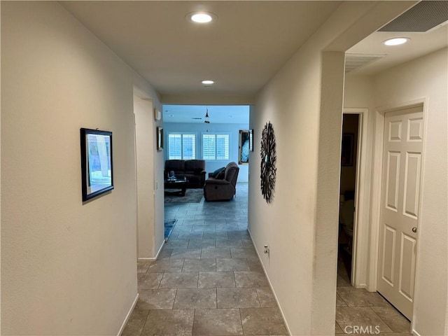 corridor featuring stone finish floor, baseboards, visible vents, and recessed lighting