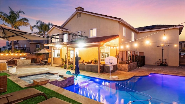 rear view of property featuring a patio, a balcony, an outdoor kitchen, solar panels, and stucco siding