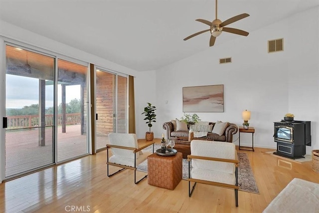 living room featuring visible vents, a ceiling fan, wood finished floors, and a wood stove