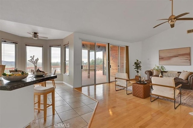 living area with ceiling fan, baseboards, vaulted ceiling, light wood-type flooring, and visible vents