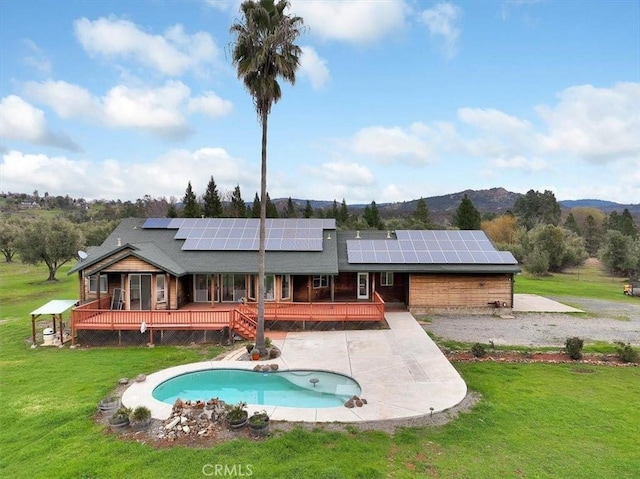 back of house featuring a deck with mountain view, an outdoor pool, solar panels, and a yard