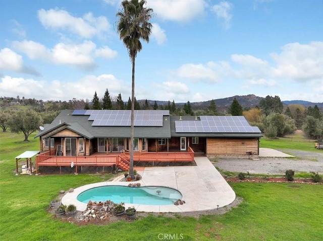 back of property with a patio, an outdoor pool, a deck with mountain view, roof mounted solar panels, and a lawn