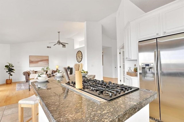 kitchen with ceiling fan, stainless steel refrigerator with ice dispenser, gas stovetop, lofted ceiling, and white cabinetry