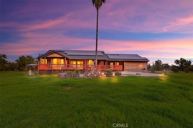 back of property featuring a lawn, roof mounted solar panels, and a porch
