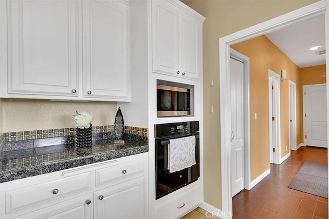 kitchen featuring black oven, tile countertops, stainless steel microwave, white cabinetry, and baseboards