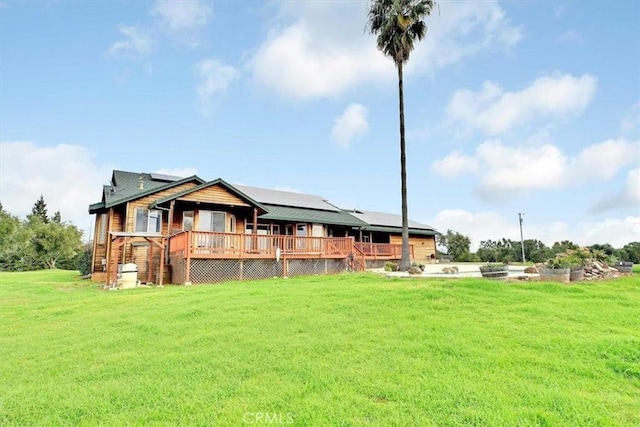 rear view of house featuring roof mounted solar panels, a wooden deck, and a yard