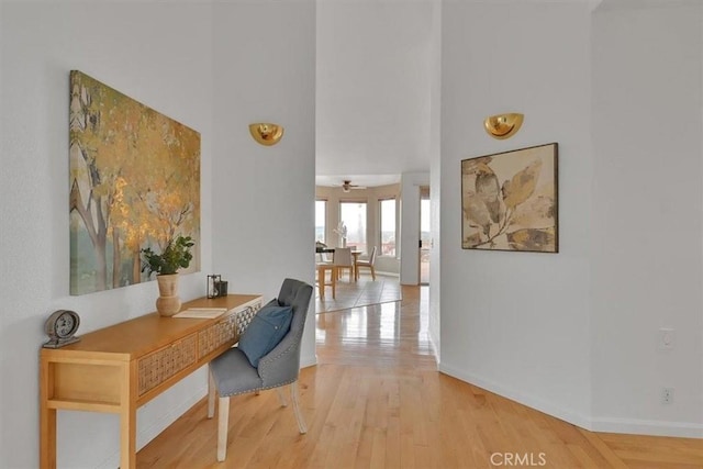 office with baseboards, ceiling fan, light wood-style flooring, and a high ceiling